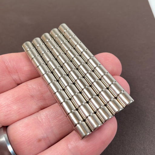 50 earth magnets lined up being held in a hand for scale