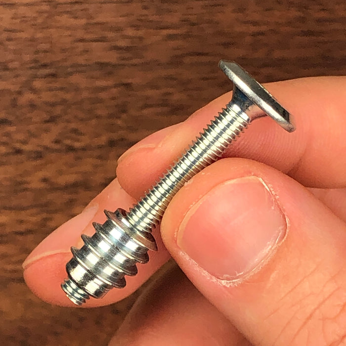 a long flat head bolt showing between two fingers and a threaded insert slightly spun and attached to the bottom